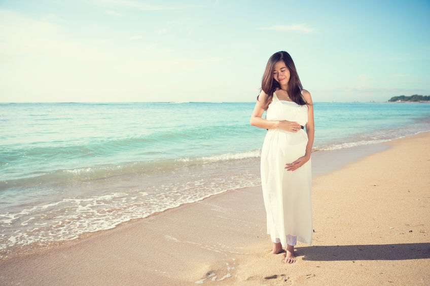 A pregnant lady walks along a beautiful beach